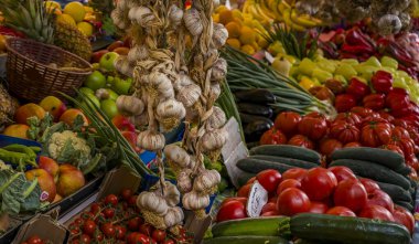Bir pazar yerinde çeşitli canlı meyve ve sebzeler sergilenerek, domates, sarımsak, biber ve salatalık gibi taze ürünlerin sergilenmesi, pitoresk ve renkli bir market sahnesi yaratıyor..