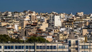 Parlak güneş ışığı altında yoğun bir apartman yığını, kent yaşamını gözler önüne seriyor. Yakın çevreyi ve şehir mimarisini vurguluyor..