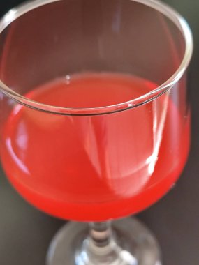 Koyu bir yüzeye yerleştirilmiş canlı kırmızı bir içeceği olan zarif bir cam bardak..