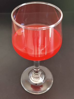 Koyu bir yüzeye yerleştirilmiş canlı kırmızı bir içeceği olan zarif bir cam bardak..