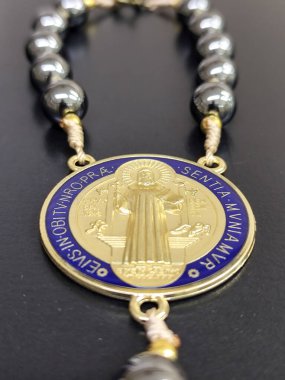 10 hematit boncuk ve altın detaylarla dolu bir Saint Benedict madalyası. Madalyonun canlı tasarımı koruma ve inancı çağrıştırıyor..