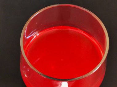 Koyu bir yüzeye yerleştirilmiş canlı kırmızı bir içeceği olan zarif bir cam bardak..