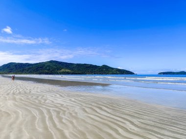 Praia da Fazenda - Ubatuba SP. Güzel ve dalgalı kumlu bir sahil, beyaz bulutlarla dolu açık mavi bir gökyüzünün altında denizin yumuşak dalgalarını yansıtıyor..