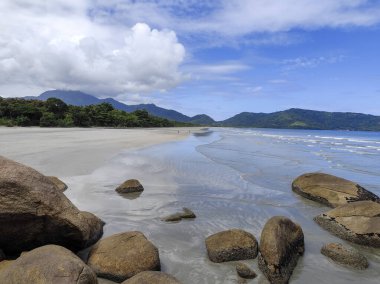 Praia da Fazenda - Ubatuba SP. Güzel ve dalgalı kumlu bir sahil, beyaz bulutlarla dolu açık mavi bir gökyüzünün altında denizin yumuşak dalgalarını yansıtıyor..