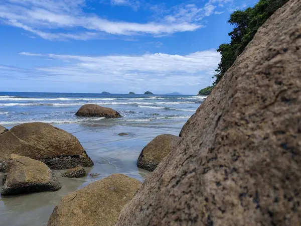 Praia da Fazenda - Ubatuba SP. Güzel ve dalgalı kumlu bir sahil, beyaz bulutlarla dolu açık mavi bir gökyüzünün altında denizin yumuşak dalgalarını yansıtıyor..
