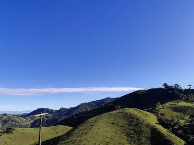 Yumuşak tepeleri ve açık mavi gökyüzü olan yeşil bir manzaranın güzel manzarası..