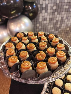 Güller şeklinde süslemelerle süslenmiş bir tepsi şekerle süslü bir parti. Arka planda gümüş ve siyah balonlar yer alıyor, şenlikli ve sofistike bir balon oluşturuyor.