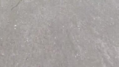 Yumuşak, doğal dokularla kumların üzerinde dalgalanan sığ sahil suyu manzarası..