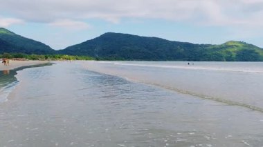 Ubatuba, Brezilya 'daki Ubatumirim Sahili' nde bulutlu bir gökyüzünün altında hafif dalgalar yuvarlanıyor..