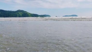 Ubatuba, Brezilya 'daki Ubatumirim Sahili' nde bulutlu bir gökyüzünün altında hafif dalgalar yuvarlanıyor..