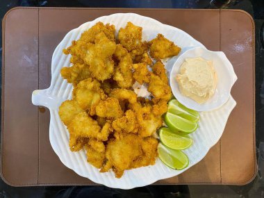 Beyaz seramik tabakta servis edilen, limon dilimleriyle süslenmiş ve yanında mayonez ile birlikte ağız sulandıran kızarmış tavuk parçaları..