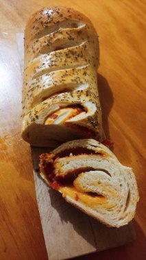 Sos ve peynirle doldurulmuş bir ekmek ahşap bir masanın üzerindedir. Tadını çıkarmaya hazır bir dilim var..