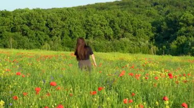 Yazın yeşil bir çayırda oturan uzun siyah saçlı genç bir kadın. Etrafı uzun otlar ve kır çiçekleriyle çevrili. Sıcak altın güneş ışığının tadını çıkarıyor..