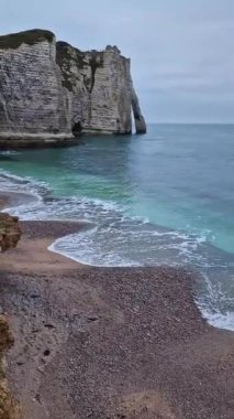Sightseeing vertical view to the wonderful cliffs of Etretat washed by the waves of the blue sea water, La Manche Channel. Famous Falaise d'Aval coastline in Normandy, France