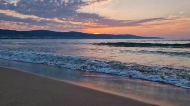 Denizde sabah, ufukta canlı bir gündoğumu ve kumlu sahile vuran köpüklü dalgalarla.