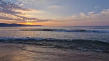 Kumlu plajı köpüklü dalgalarla yıkayan canlı deniz gündoğumu. Güneşin ufukta yükseldiği şafak sahnesi.