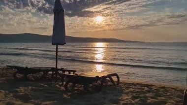Kumsaldaki tatil köyünde güneşli yataklar ve şemsiyelerle gün doğumu. Yaz tatili deniz kenarı, seyahat konsepti