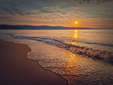 Huzurlu deniz manzarası, sakin bir sabah denizi tepelerin üzerinde güzel bir gün doğumu ve kuma vuran köpüklü dalgalar. Denizde şafak, yolculuk geçmişi
