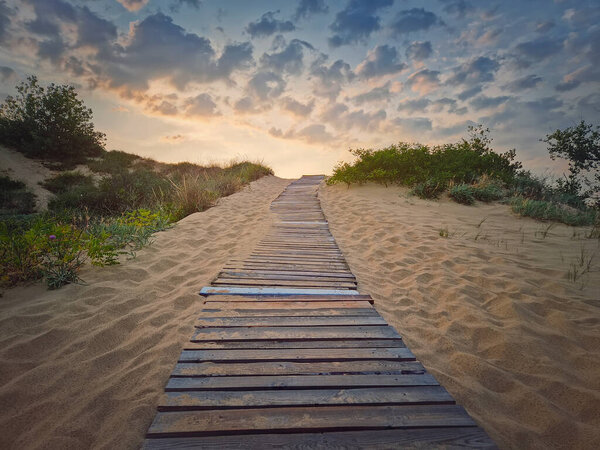 Wooden path through the sand leading to the beach. Beautiful morning sky with fluffy clouds