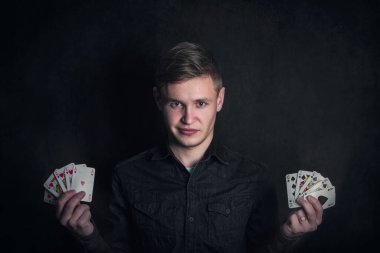 Kumarbaz iki elinde de iskambil kâğıdı tutuyor. Floş floş başarılı poker kombinasyonları. Kumarhane oyunları turnuvası reklamı. Şanslı oyuncu ya da sihirbaz karanlık arka plana karşı numaralar gösteriyor