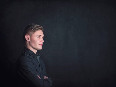 Olumlu düşünen genç adam portresi, kollarını siyah bir duvar arkasında çapraz tutarak kendinden emin görünüyor. Erkek öğrenci iyimserlikle yansıyor