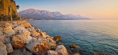 Kemer kıyı şeridinin panoramik manzarasında görkemli Taurus dağları sabah güneş doğarken sakin denizin üzerinde yükseliyor. Türkiye Akdeniz kıyısı manzarası
