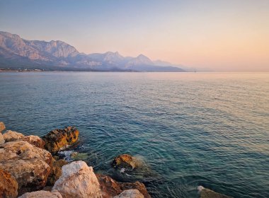 Kemer kıyı şeridi manzaralı görkemli Taurus dağları sabah güneş doğarken sakin denizin üzerinde yükseliyor. Türkiye Akdeniz sahili manzarası