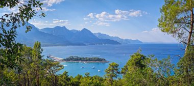 Panoramik Kemer kıyı manzarası. Arkasında görkemli Taurus dağları olan canlı deniz manzarası. Ay Işığı Sahili 'ne ve hareketli bir limanı olan yarımadaya en üst manzara. Türkiye 'de yaz tatili