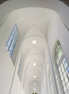 Yüksek çözünürlüklü beyaz, modern bir koridor, yüksek kubbeli bir tavan, büyük pencerelerle aydınlatılmış ve arka arkaya asılmış minimalist küresel kolyeler serisi.