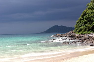 Bir deniz manzarasının fotoğrafı. Adadan sahile, okyanusa ve gökyüzüne bak. Gökyüzü bulutlu. Deniz, kum, kayalar ve fırtına.