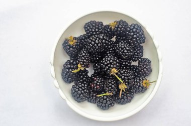 Arka planda beyaz bir tabakta siyah sulu böğürtlen. Böğürtlen manzarası.