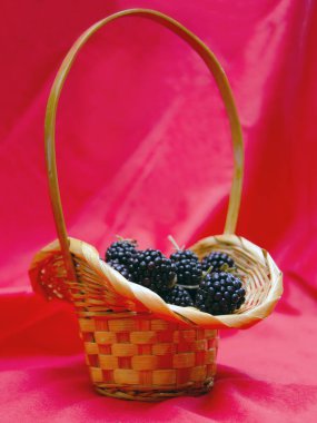 Kırmızı arka planda sepetlerde siyah, sulu böğürtlenler. Sepette böğürtlen