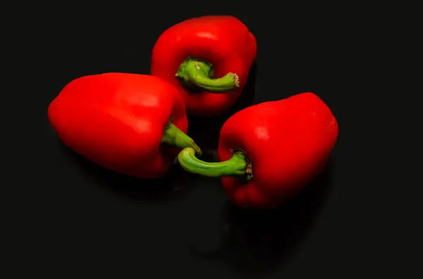 Red pepper. Several ripe red bell peppers on a black background, vegetables, sweet pepper