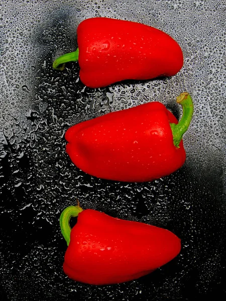 Red pepper. Several ripe red bell peppers with dew drops on a dark background, vegetables, sweet pepper