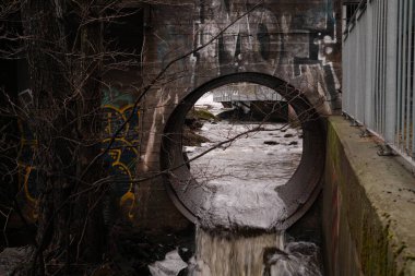 Duvarında grafiti olan bir tünel ve su sızdıran bir boru. Sahne karanlık ve ürkütücü.