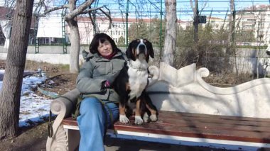 Bir kadın ve köpeği güneşlenir, kış günü bir bankta oturur ve birbirlerine sarılırlar.