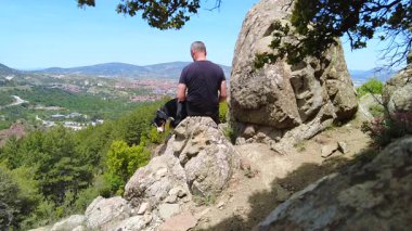 Bir adam ve köpeği dağların tepesinde vahşi doğanın güzelliğine hayran kalarak rahatlarlar..