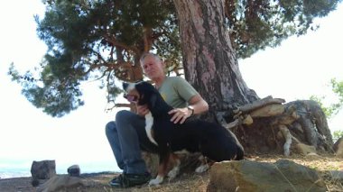 Bir Entlebucher Dağ Köpeği ve sahibi sıcak bir yaz gününde büyük bir ağacın gölgesinde oturup harika bir yürüyüşten sonra dinlenirler..