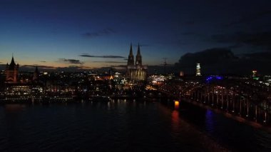 Almanya 'nın güzel şehri Köln' ün hava klibi. Gece günbatımından hemen sonra. Drone uçuyor. Videoda ünlü katedral Dom, Rhein nehri, Hohenzollernbrcke köprüsü ve güzel yıldırımlarla dolu eski şehrin geri kalanı gösteriliyor..