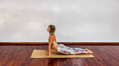 Kadın yoga stüdyosunda yukarı bakan köpek pozu veriyor. Herkes için basit ve müsait. Urdhva mukha shvanasana egzersizi