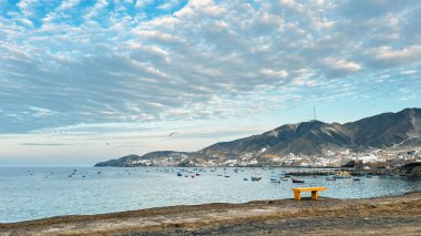 Pasifik Okyanusu 'nda sakin bir körfez, küçük bir liman ve bir sürü küçük balıkçı teknesi var. Boş bank, Peru 'daki Tortuga Sahili' nin arka planındaki liman ve dağları gösteriyor