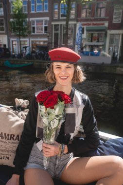 Askeri kırmızı bereli güzel bir kadın kameraya bakıyor ve mutluluğunu kırmızı güllerden ve Amsterdam 'da turist olarak mükemmel bir zaman geçirdiğini söylüyor.