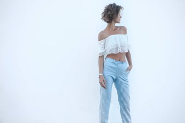 Beyaz arka planda güzel bir genç kadın, kopyalama alanı, mesaj için boş yer. Zarif model yana bakıyor, şık yaz kıyafetleri giyiyor omuzları açık ve çizgili pantolonları var..