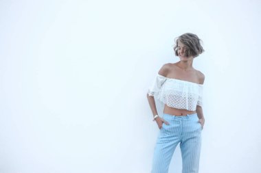 Beyaz arka planda güzel bir genç kadın, kopyalama alanı, mesaj için boş yer. Şık bir model, şık bir yaz elbisesi, omuzları açık ve çizgili pantolonları var..