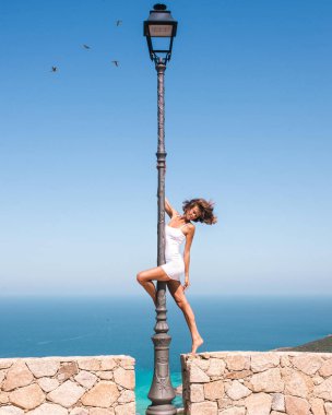 Erkekle dans eden güzel bir kadın ama Corsica 'da Akdeniz manzarası önünde beyaz kısa elbiseli eski moda sokak lambasıyla dans ediyor. Yaz boyunca Avrupa 'da seyahat eden dansçı.