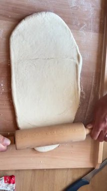 Tahta bir masa üzerinde hamuru ahşap bir raptiyeyle yuvarlayan bir adamın video görüntüleri. Ev yapımı pişirme, adım adım aşçılık dersi, hazırlık, pasta