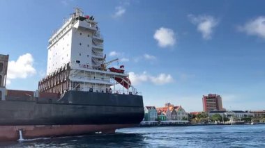 Büyük bir kargo gemisinin ortadan kaybolmasıyla, başkent Curacao Willemstad 'da Hollanda tarzı koloni renkli evlerin güzel manzarası açılıyor.