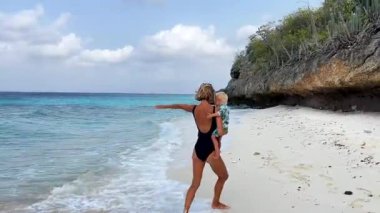 Genç anne, kucağında küçük çocuğuyla yalnız Karayipler sahilinde koşuyor, oynuyor ve etrafında dönüyor. Annem küçük bebekle gezintiye çıkmaktan hoşlanıyor.