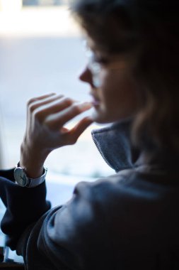 Zarif, karanlık bir ortamda güzel bir kadının portresi okuma gözlüğü takıyor ve büyük bir pencerenin önünde otururken kameraya bakıyor. Eline odaklan ve izle.