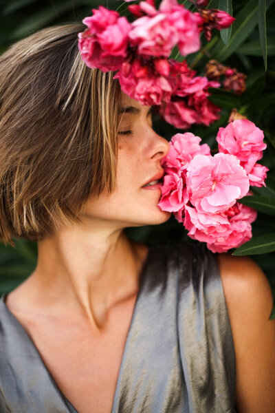 Head shot of fashion model smelling on beautiful pink flower. Natural beautiful woman with no make up with blossoms, cosmetics concept, natural beauty, skin care
